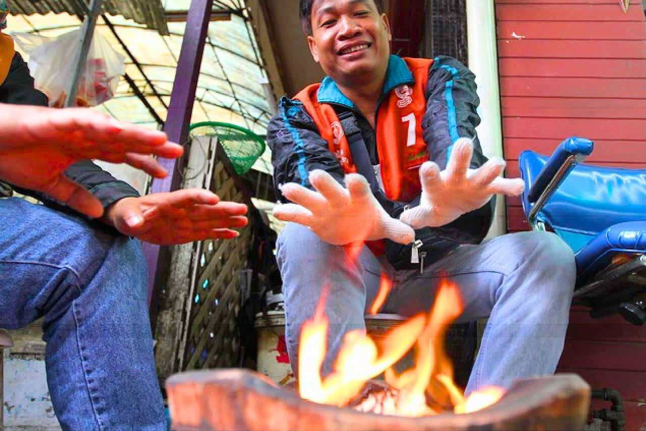 Des chauffeurs de moto-taxi se réchauffent autour d'un feu en Thaïlande.